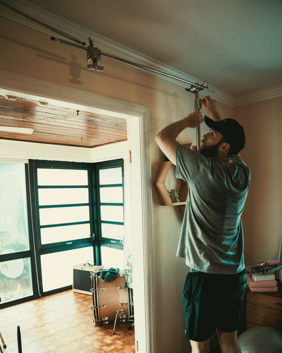 A tradesman in a cap fitting a fixture above a doorway in a sunny room