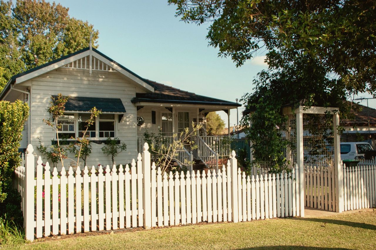 A white weatherboard home with a picket fence and a leafy garden on a sunny day