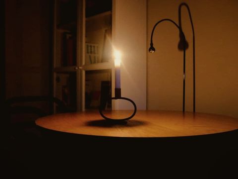 A lit candle on a table beside a desk lamp that is switched off