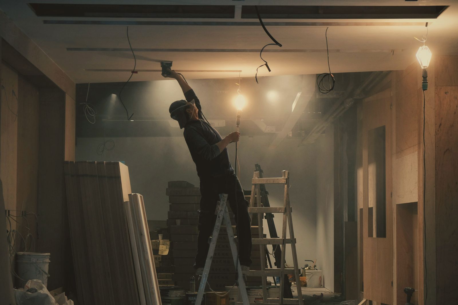 An electrician on a stepladder running cable across a ceiling in a room being renovated